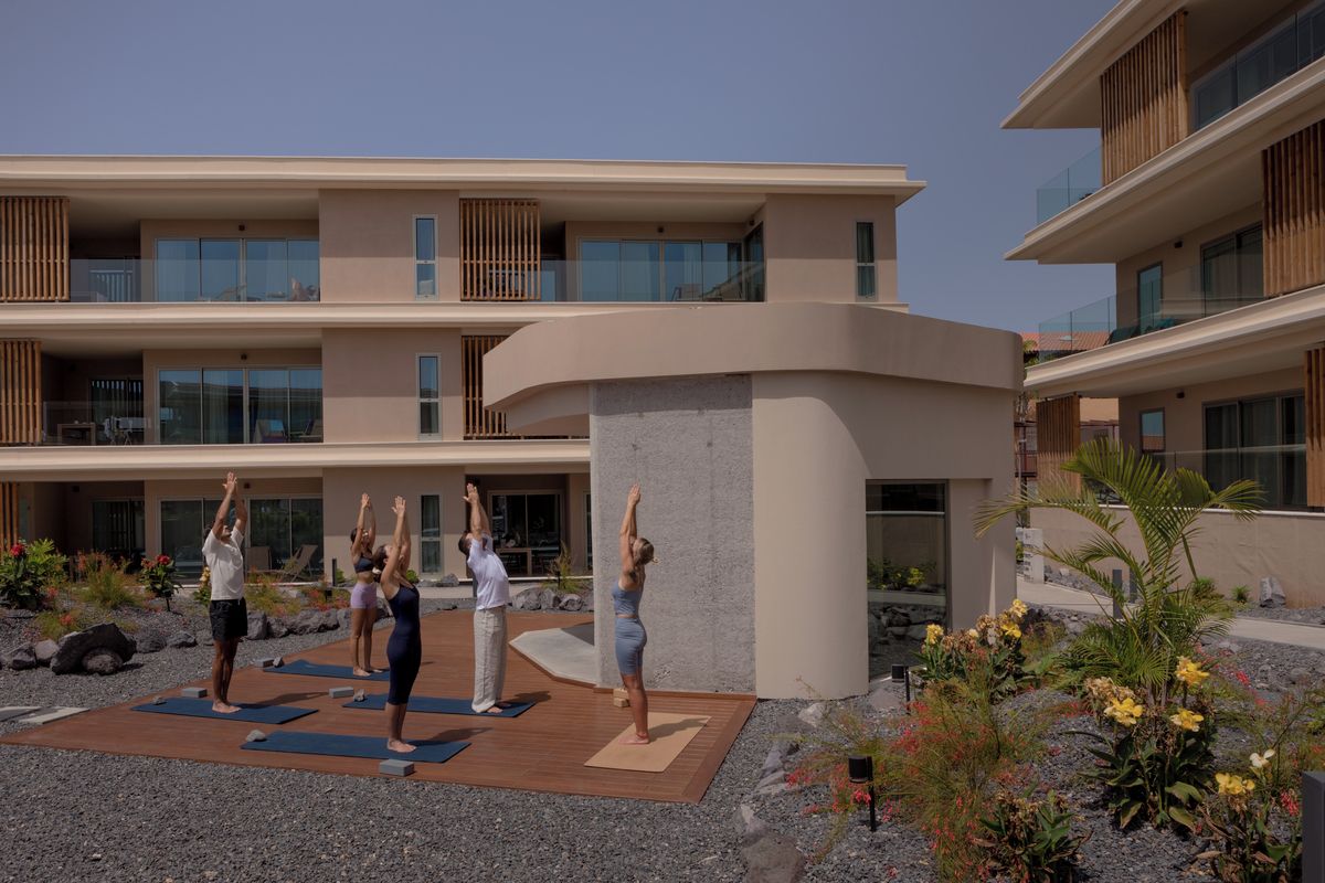 Un edificio de varios pisos con balcones, un patio con tapetes de yoga y jardines ajardinados.
