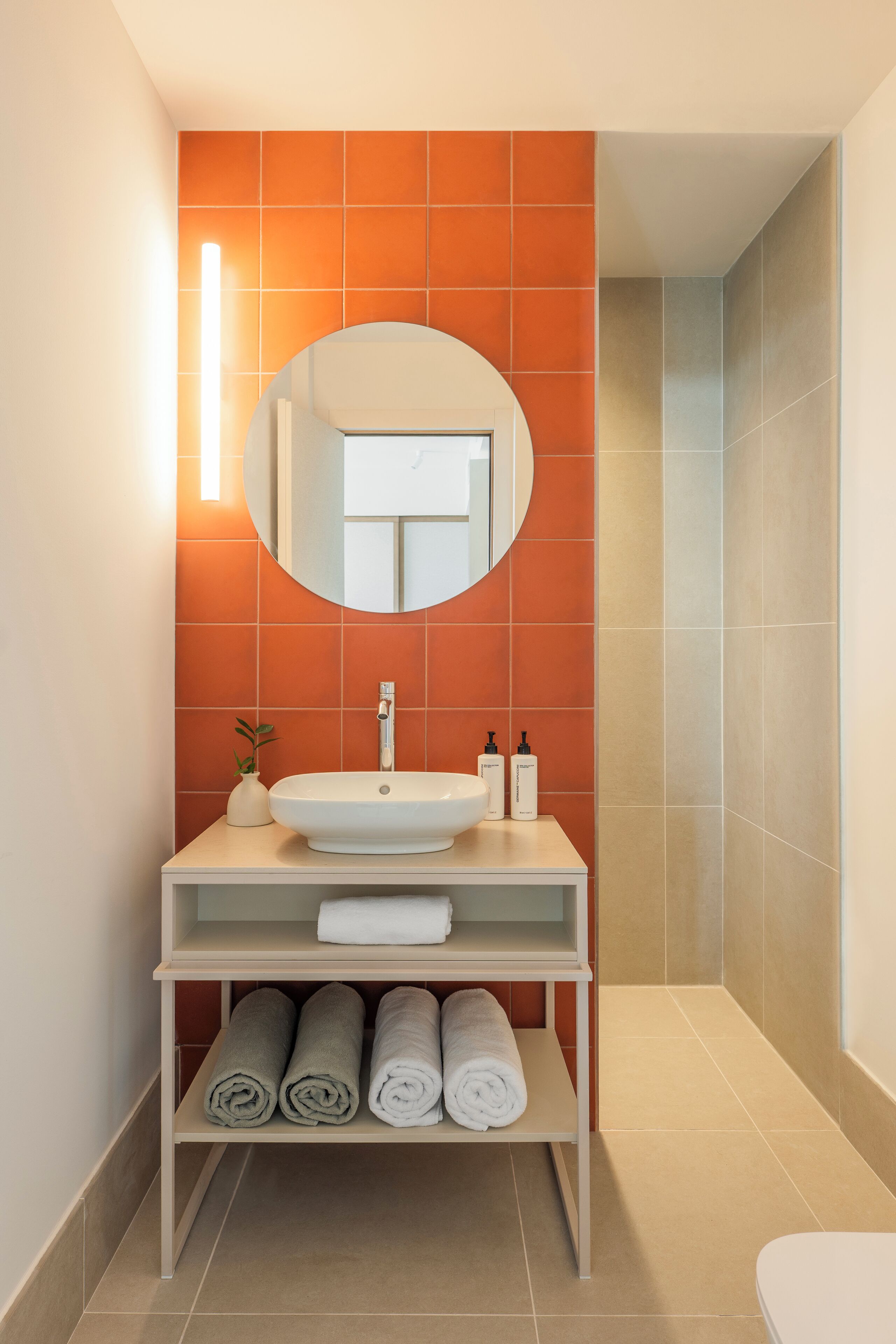 A bathroom with a white sink, a round mirror, and orange tiles.