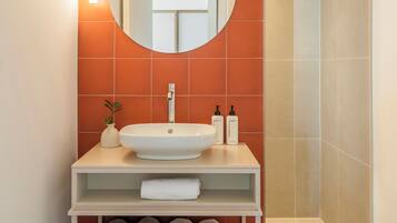 A bathroom with a white sink, a round mirror, and orange tiles.