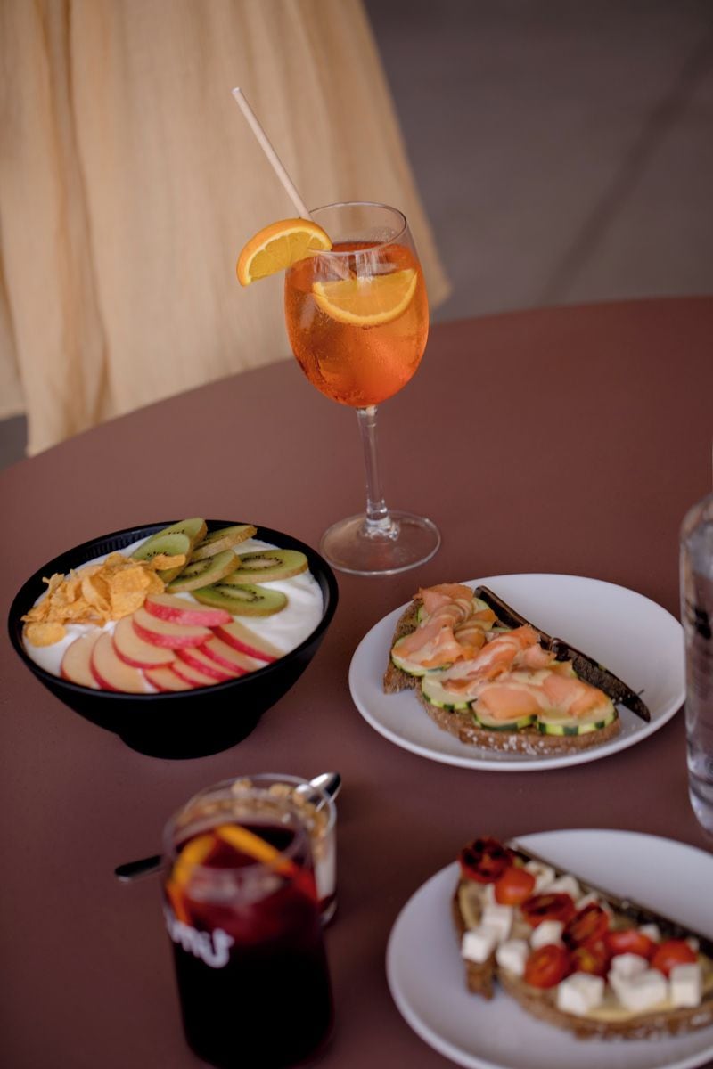 Ein Tisch mit einem Glas Eistee, einer Schüssel Joghurt mit Früchten, einem Teller mit Lachs und einem Glas rotem Getränk.