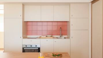 A modern kitchen with white cabinets, a pink backsplash, and a wooden table with a glass of orange juice and a plate of food.