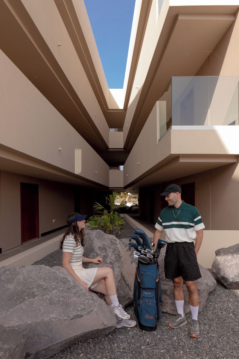 Un edificio moderno con un área exterior cubierta, rocas grandes y un bolso de golf.