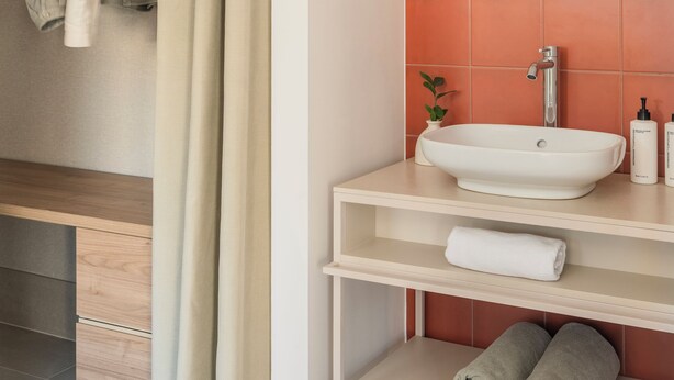 Un baño con un lavamanos color beige, un espejo y un perchero para toallas.