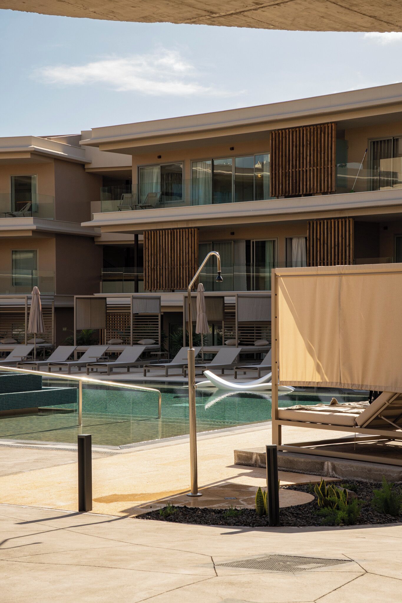 A modern hotel with a pool area, lounge chairs, and a covered seating area.