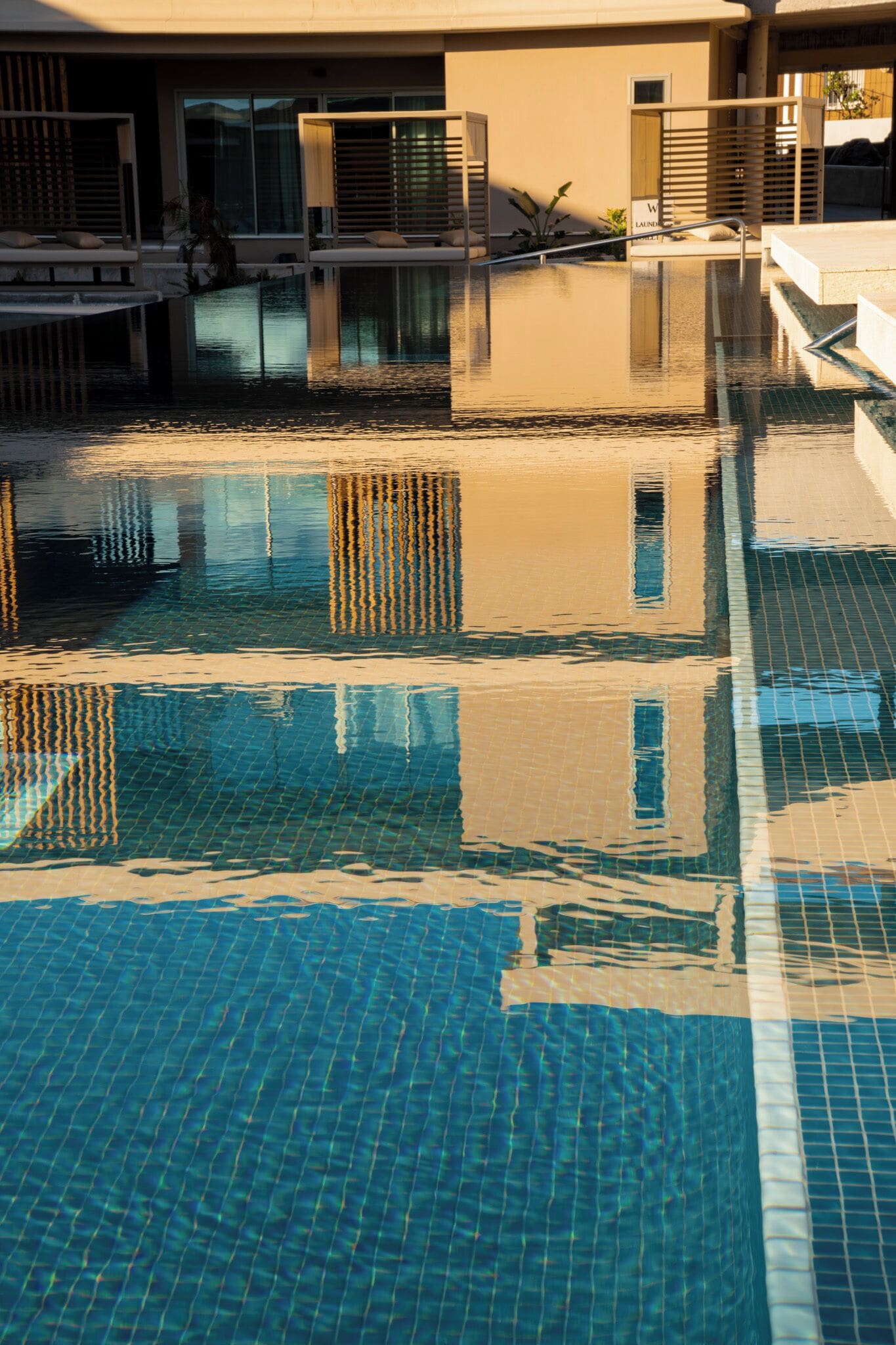 Ein Schwimmbecken mit klarem, blauem Wasser, einer gefliesten Liegefläche und ein Gebäude mit großen Fenstern im Hintergrund.