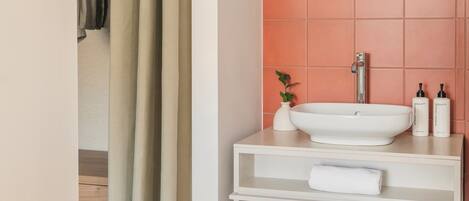 Un baño con un lavamanos blanco, un espejo redondo y un estante con toallas.