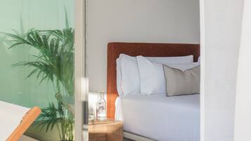 Een hotelkamer met een bed, een nachtkastje, een waterfles en een potplant.