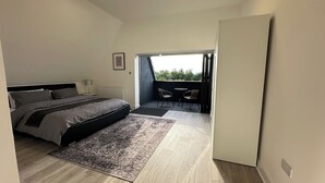 A bedroom with a large bed, a nightstand, a chair, and a view of the outdoors through a door. - Luxurious New House Near Manchester Airport (Wythenshawe)