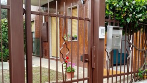 Una entrada protegida con un portón metálico, una planta en maceta y un cuadro de electricidad.