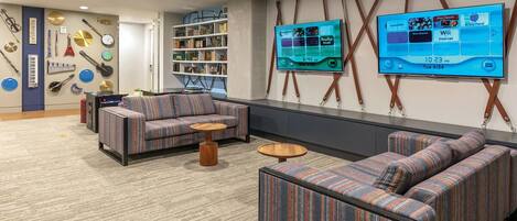 A modern lounge area with striped sofas, a bookshelf, and a large flat-screen TV displaying a schedule.