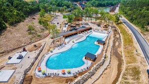 Un resort con una gran piscina, zonas de descanso y vistas a las colinas boscosas circundantes.