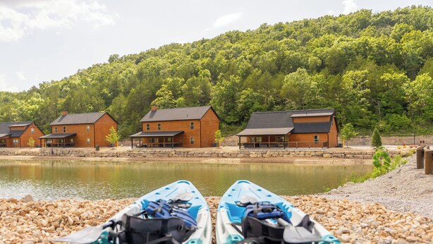 Vista de un lago con cabañas de madera y kayaks sobre piedras.