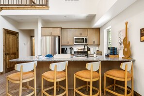 A modern kitchen with a central island, stainless steel appliances, and wooden bar stools.