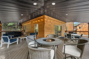 A covered outdoor area with a fire pit, seating, and a grill.