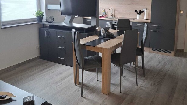 Una cocina moderna con comedor, que cuenta con una mesa y sillas de madera, televisión integrada y un ventanal con vistas al exterior.