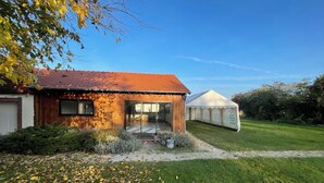 Ein rustikales Haus mit rotem Ziegeldach, einem Glastür-Eingang und einem weißen Zelt im Hintergrund.