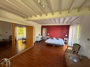 A spacious bedroom with a large bed, a wooden floor, a desk, and a chair.
