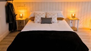 A bedroom with a bed, two bedside tables, a hanging coat rack, and a wall with a sign. - Lorraine's Loft - Hot Tub Get Away. Stunning countryside Views! (Cookstown)