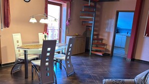 A modern living room with a dining area, a staircase, and a kitchen visible through an open door.