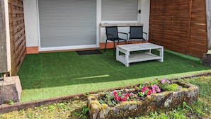 Une terrasse avec un revêtement de gazon synthétique, deux chaises, une petite table et une clôture en bois.