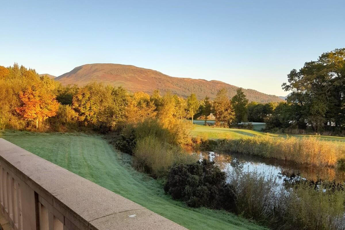 A bridge with a view of a river, trees, and hills in the background.