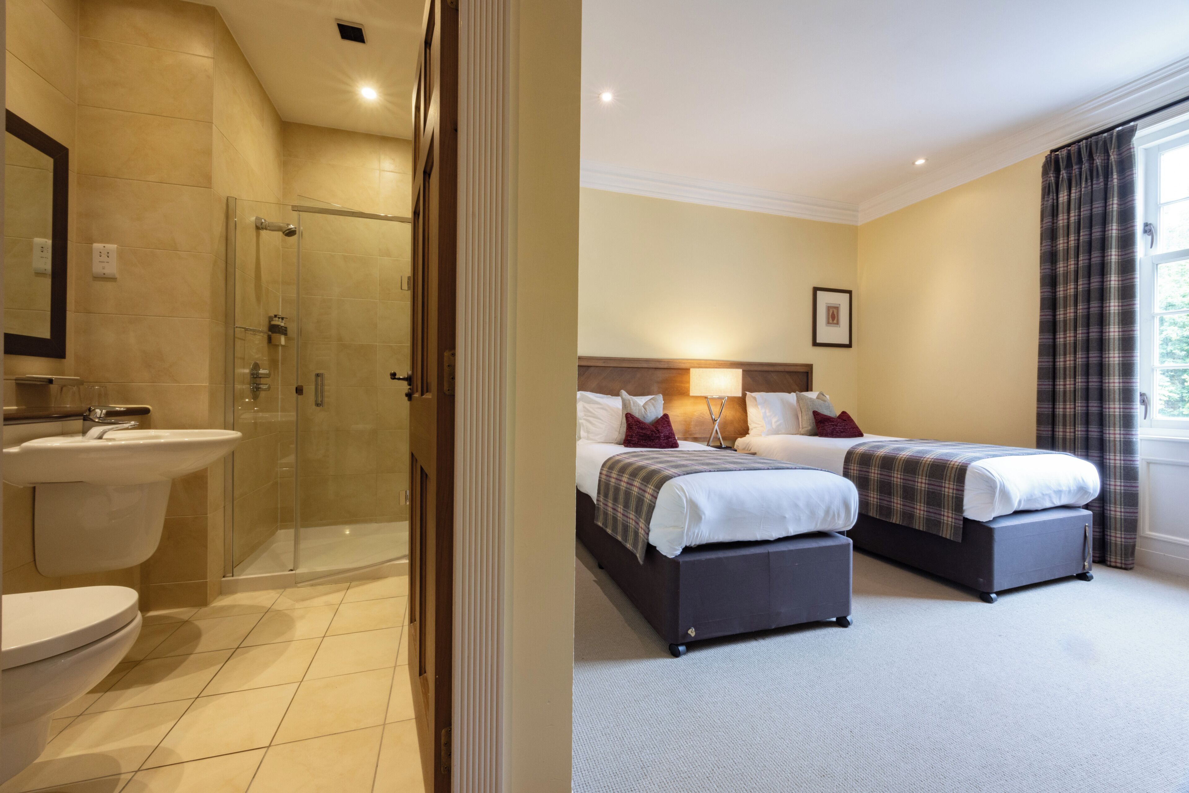Une chambre d’hôtel avec une douche, un lavabo, deux lits et une fenêtre avec des rideaux.