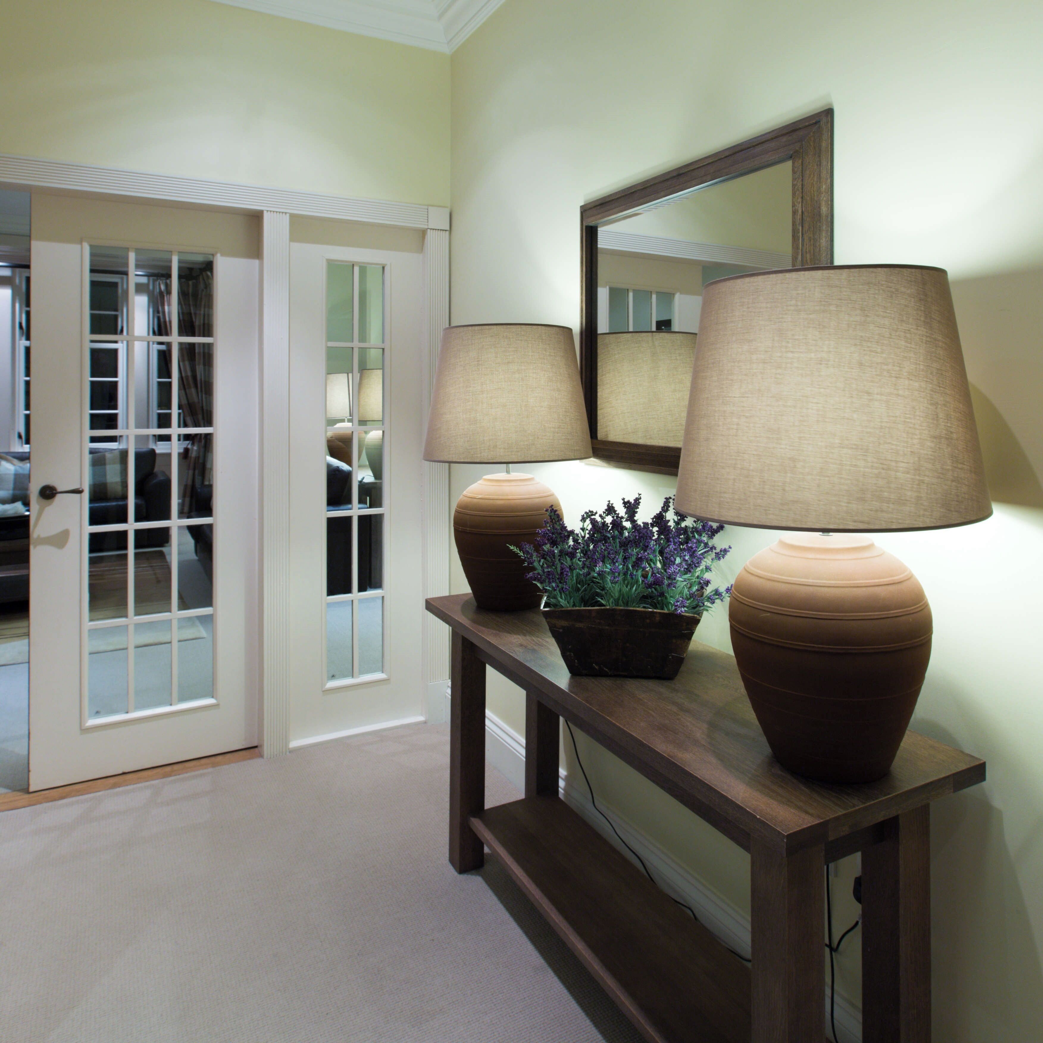 A hallway with a wooden console table, two lamps, a potted plant, and a mirror on the wall.