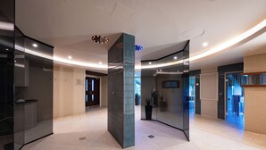 A modern hotel lobby with a curved ceiling, glass partitions, and a central column. - Mansion House Apartments at Cameron Lodges (Alexandria)