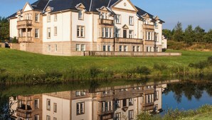 A large, multi-story building with a symmetrical facade, large windows, and a reflection in a body of water. - Mansion House Apartments at Cameron Lodges (Alexandria)