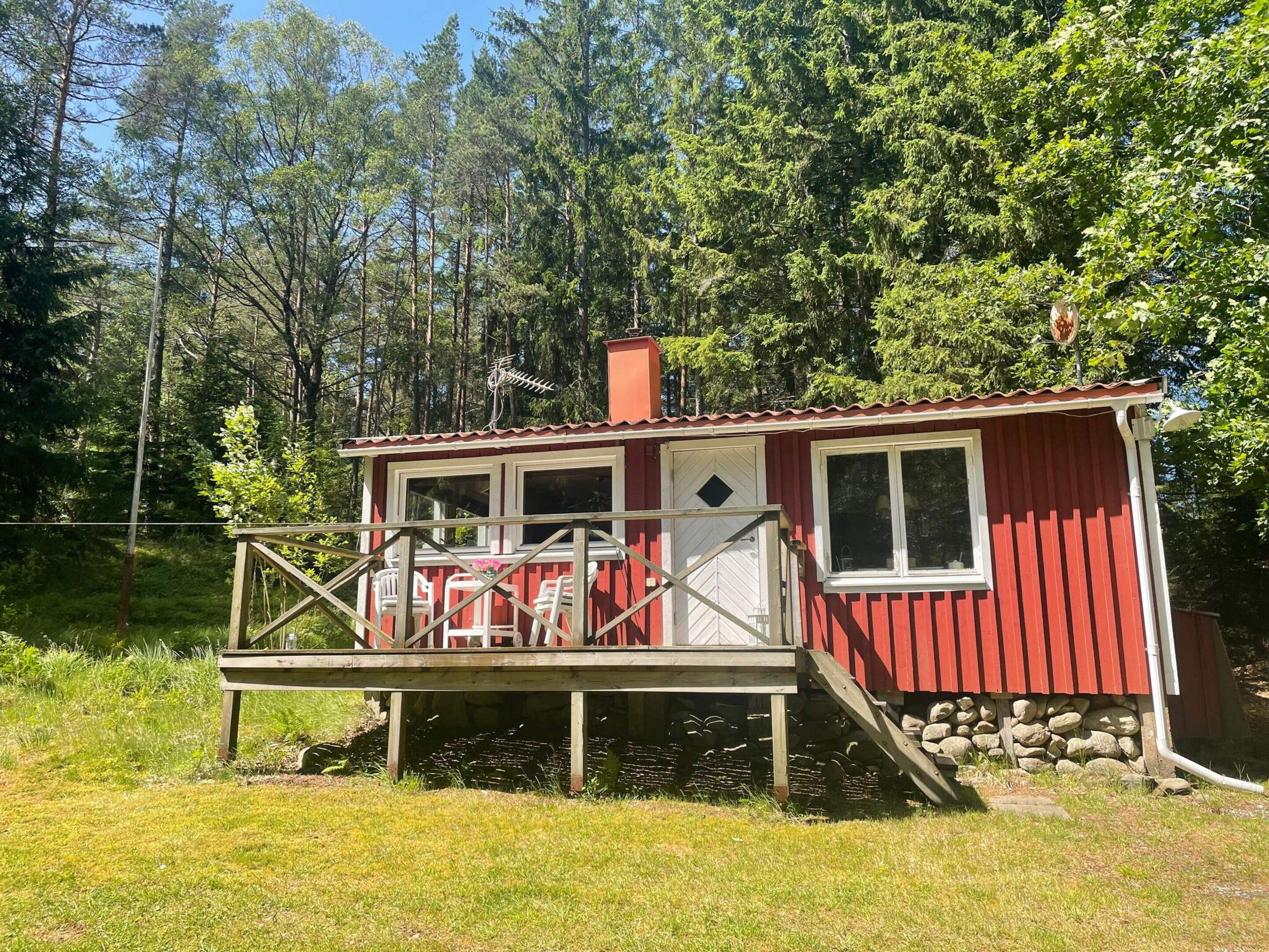 A red cabin with a deck, surrounded by trees.