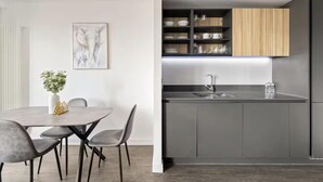 Eine moderne Küche mit grauen Schränken, einem hölzernen oberem Regal und einer Essecke mit Tisch und Stühlen.