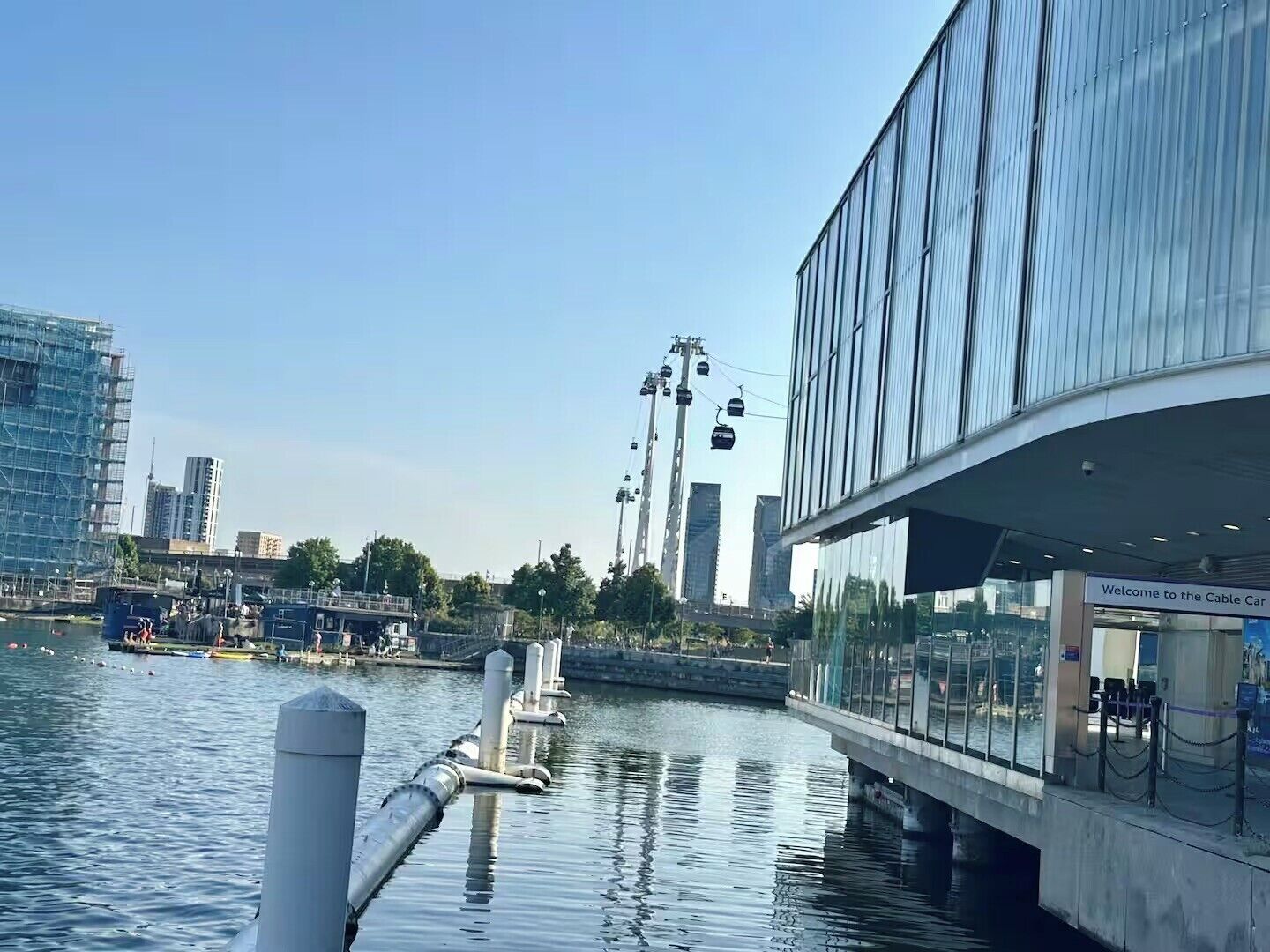 Un bâtiment situé au bord de l’eau, doté d’une façade en verre, d’un système de téléphérique et d’une  étendue d’eau au premier plan.