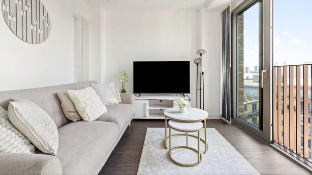 Ein modernes Wohnzimmer mit einer Couch, einem Fernseher, einem kleinen Tisch und einem Balkon mit Blick auf die Stadt.