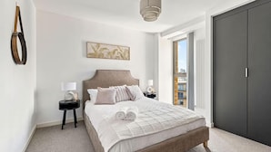 Ein Schlafzimmer mit einem großen Bett, einem Nachttisch, einer Wandlampe, einem gerahmten Bild und einem dunklen Kleiderschrank.
