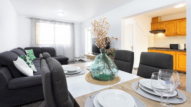 Una sala de estar moderna con comedor, una cocina al fondo y un amplio ventanal con cortinas.