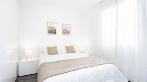 Una habitación de hotel con una cama grande, dos mesitas de noche con lámparas y una ventana con cortinas translúcidas.