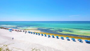 A beach with white sand and clear blue water. There are blue umbrellas and people on the beach. - Blue Mountain Beach Villas 5A (Santa Rosa Beach)