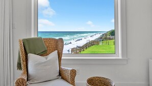 A room with a view of a beach, a wicker chair, a cushion, and a basket. - Blue Mountain Beach Villas 5A (Santa Rosa Beach)