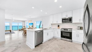 A modern kitchen with white cabinets, stainless steel appliances, and a view of the ocean. - Blue Mountain Beach Villas 5A (Santa Rosa Beach)