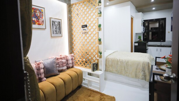 Un dormitorio moderno con sofá, cama y una zona de cocina visible a través de una puerta abierta.