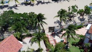 An aerial view of a resort with palm trees, a pool, and a red-roofed building.