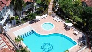 A swimming pool with a sun emblem, surrounded by lounge chairs and palm trees.