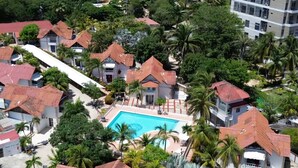 An aerial view of a residential area with multiple houses, a central swimming pool, and surrounding palm trees.