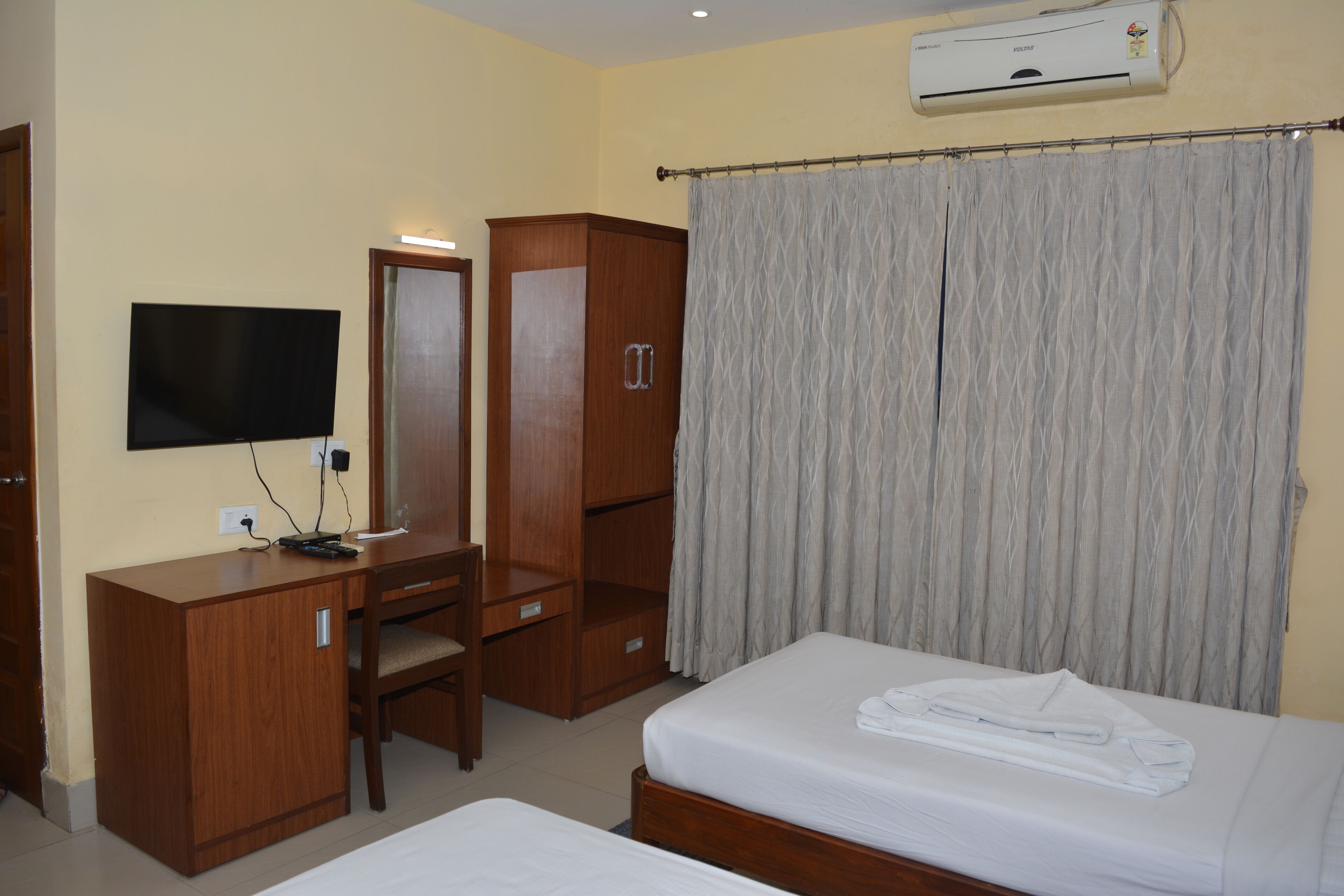 Habitación de hotel con cama, escritorio, silla, televisor, armario y cortina.