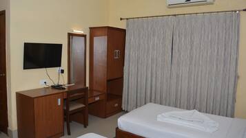 Habitación de hotel con cama, escritorio, silla, televisor, armario y cortina.