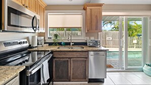 Une cuisine moderne avec des meubles en bois, des appareils en acier inoxydable, un plan de travail en granit et une vue sur un jardin avec une piscine.