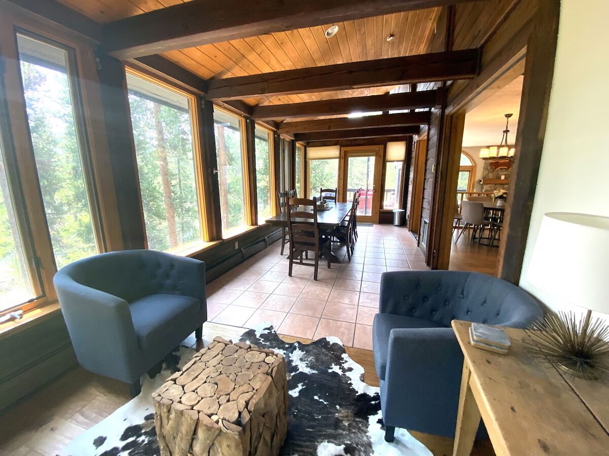 A spacious room with large windows, a dining area, and a cozy seating arrangement with two armchairs and a wooden coffee table.