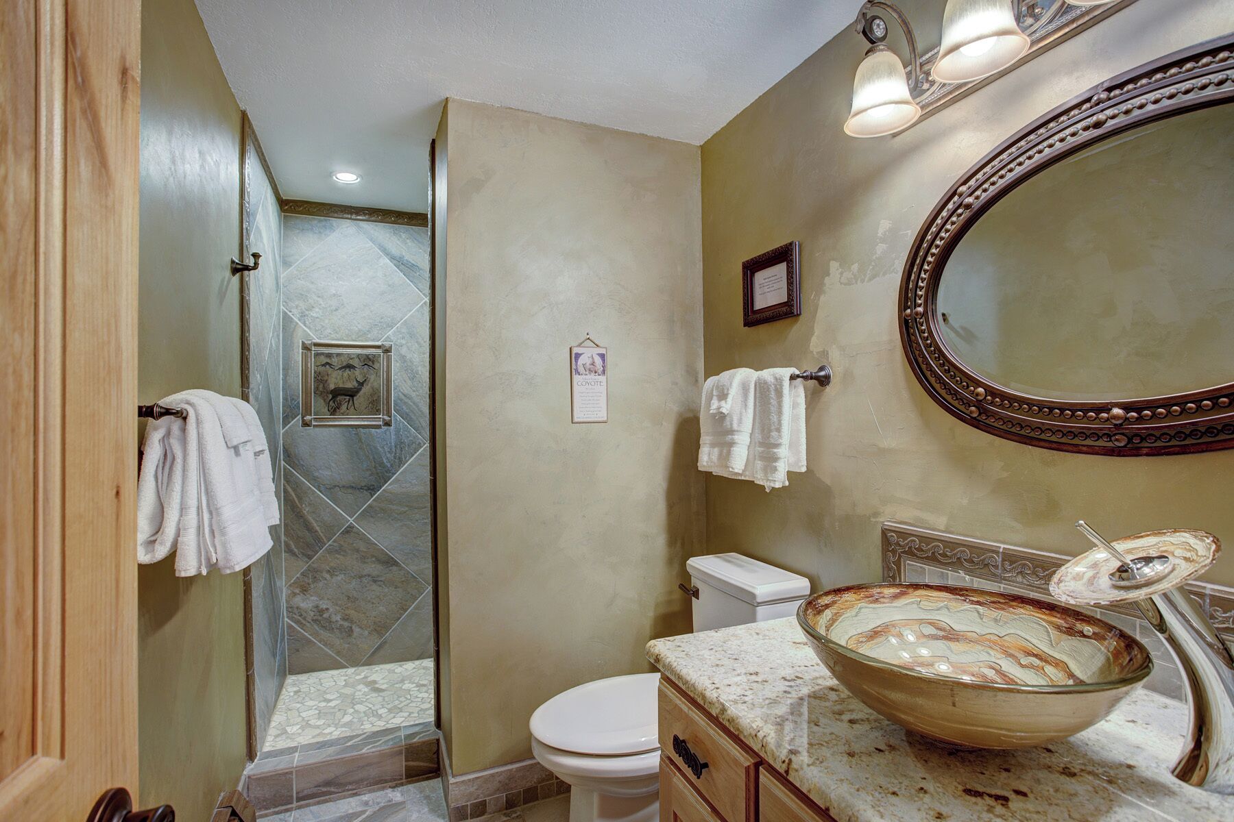 A bathroom with a glass bowl sink, a toilet, a shower with a glass door, and a mirror with a decorative frame.