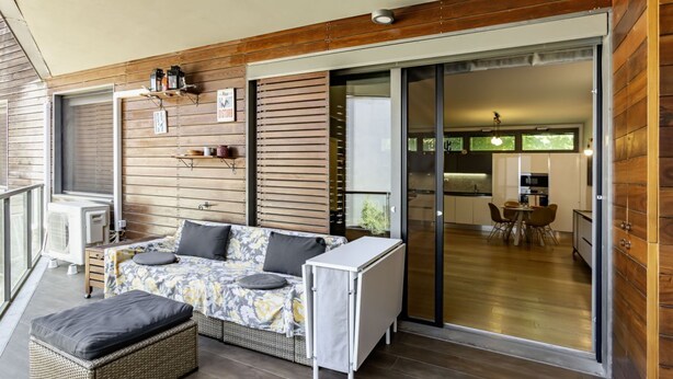 A modern interior with a sofa, ottoman, and a small table, wooden paneling, and a sliding glass door leading to a kitchen. - GuestHost - Modern Apartament with large terrace (Florence)