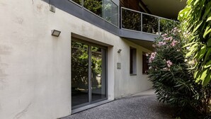 A modern building with a large sliding glass door entrance, a balcony with glass railings, and a gravel pathway. - GuestHost - Modern Apartament with large terrace (Florence)